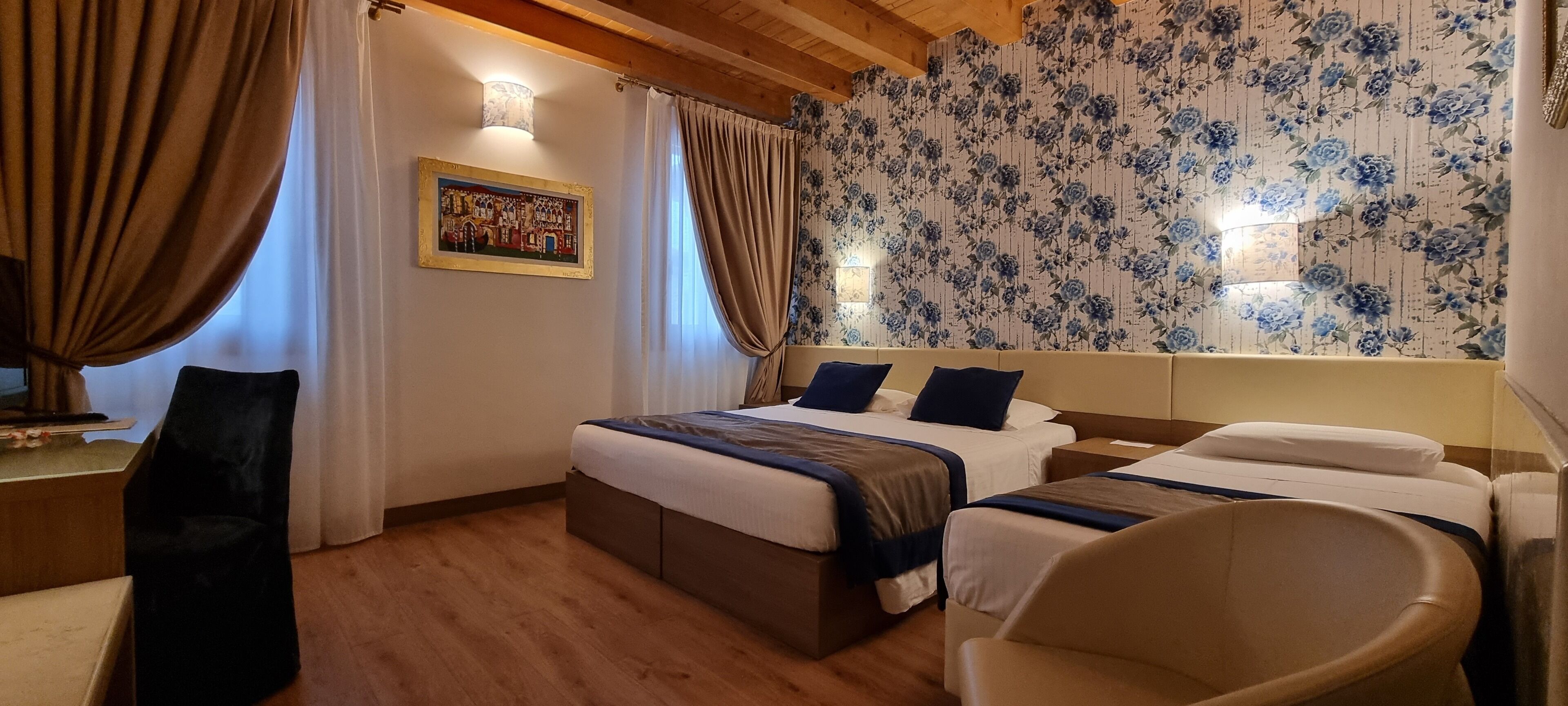 Une chambre d’hôtel avec un grand lit, deux tables de chevet, une chaise et un mur recouvert d’un papier peint à motifs floraux.
