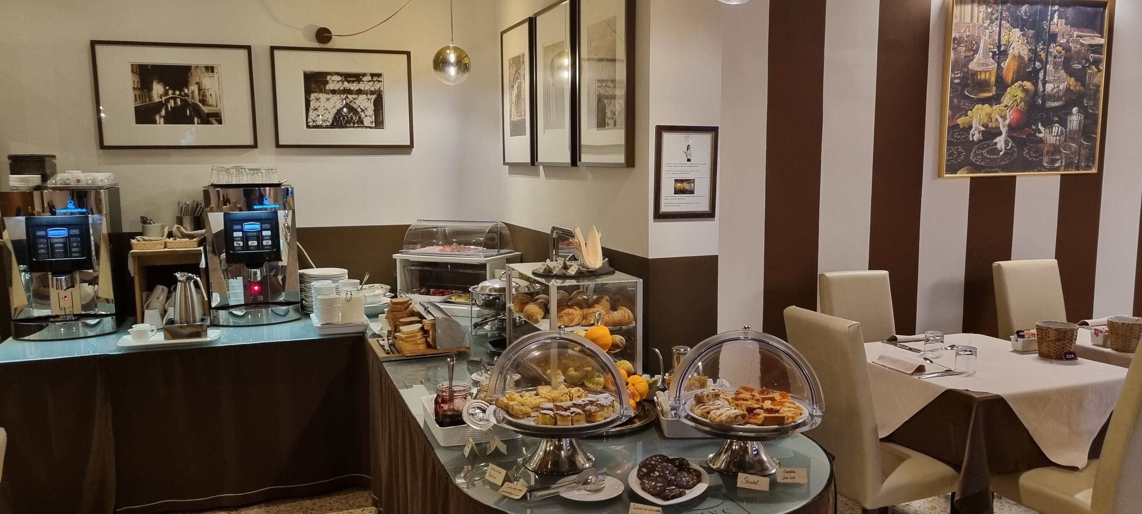 Ein reichhaltiges Frühstücksbuffet mit verschiedenen Speisen, Kaffeeautomaten und gerahmten Bildern an den Wänden.