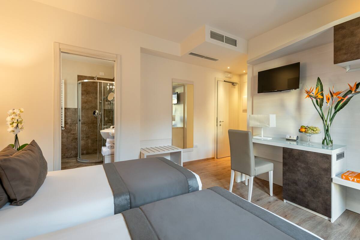 A modern hotel room with a bed, desk, and shower area.