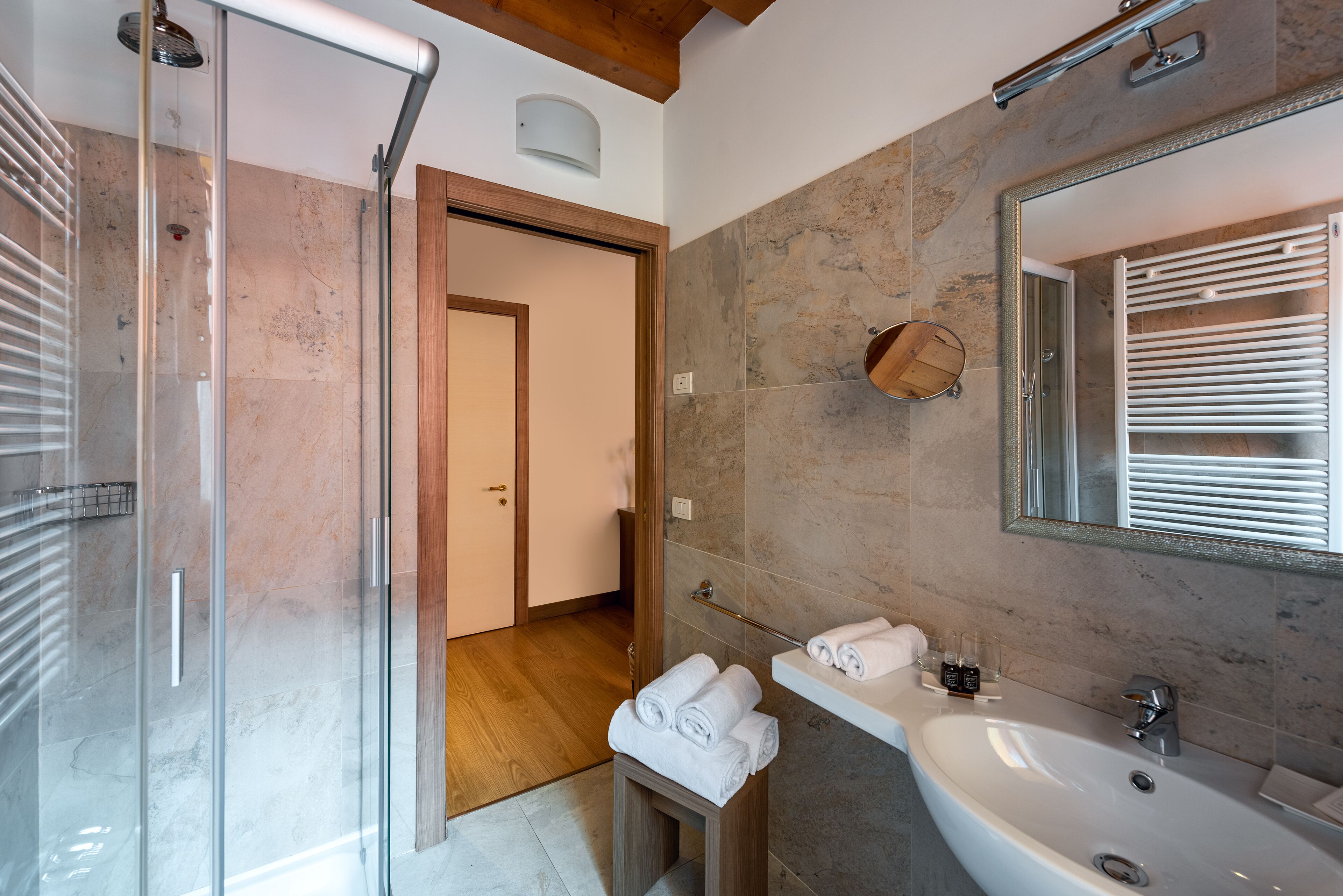 A modern bathroom with a glass shower enclosure, a wooden door, a white sink with a mirror, and a towel rack.