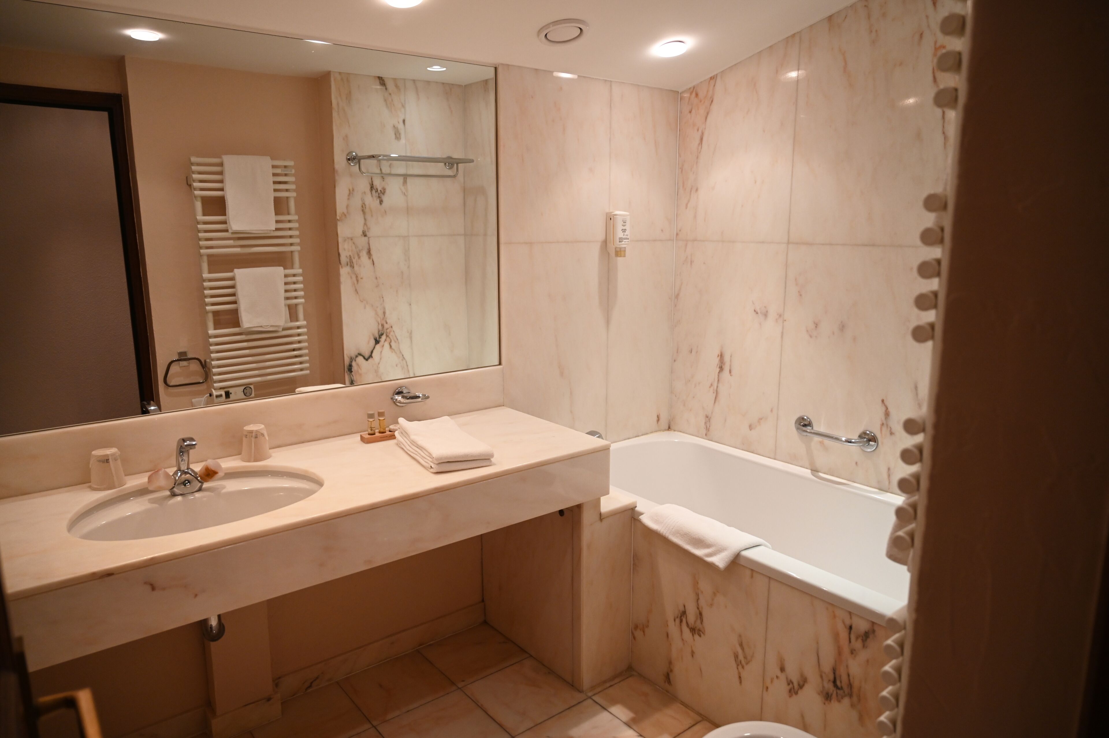A modern bathroom with a marble sink, a large mirror, a bathtub, and a towel rack.
