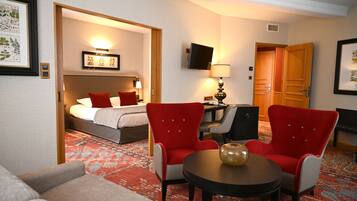 A hotel room with a bed, two red armchairs, a small table, a TV, and a patterned carpet.