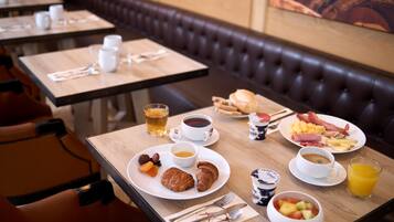 Una mesa para dos servida con desayunos, incluyendo cruasanes, fruta, café y zumo.