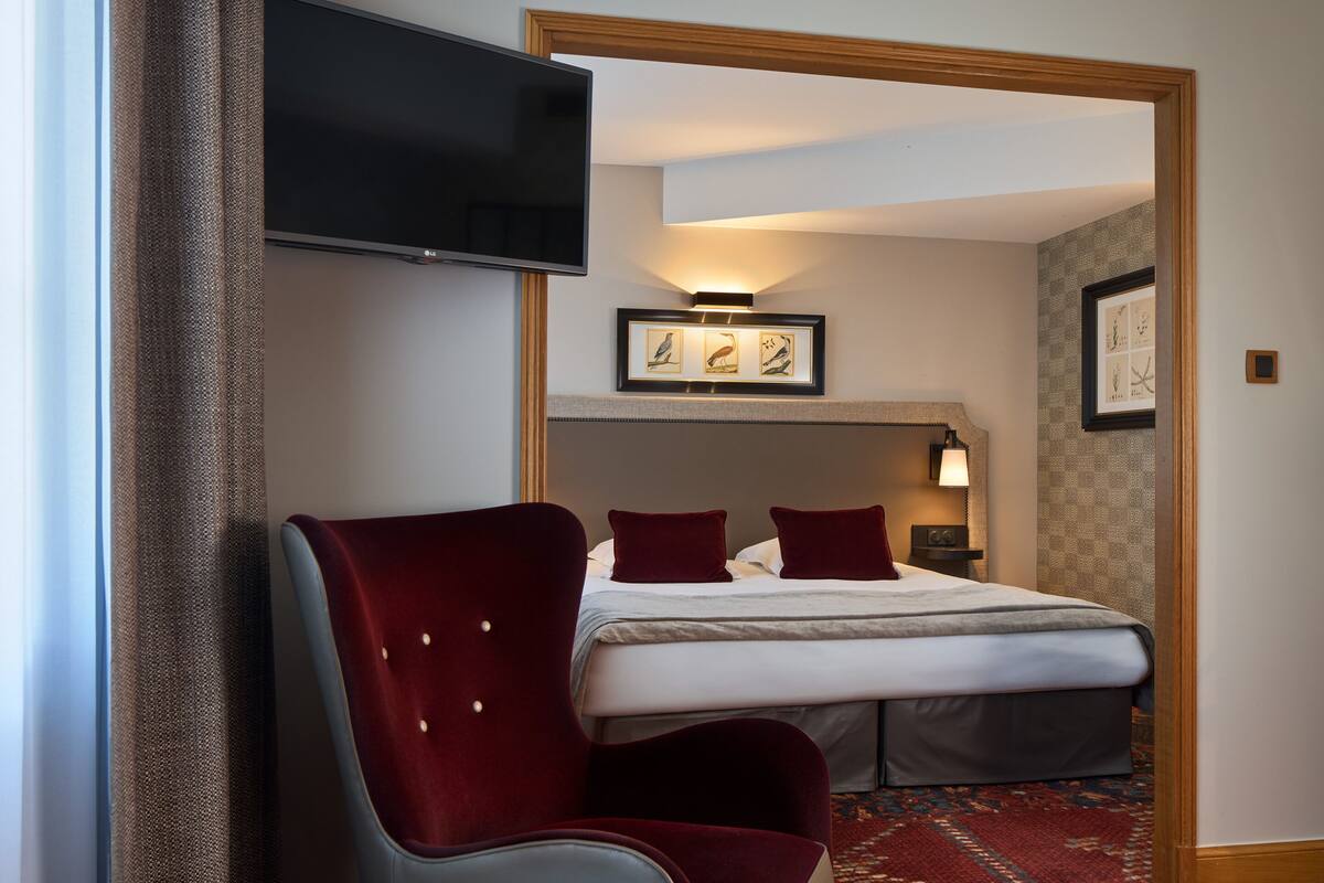 Une chambre d’hôtel avec un lit, un téléviseur fixé au mur, une chaise et un tableau encadré au-dessus du lit.