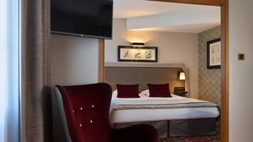 Ein Hotelzimmer mit einem Bett, einem an der Wand befestigten Fernseher, einem Sessel und einem gerahmten Bild über dem Bett.