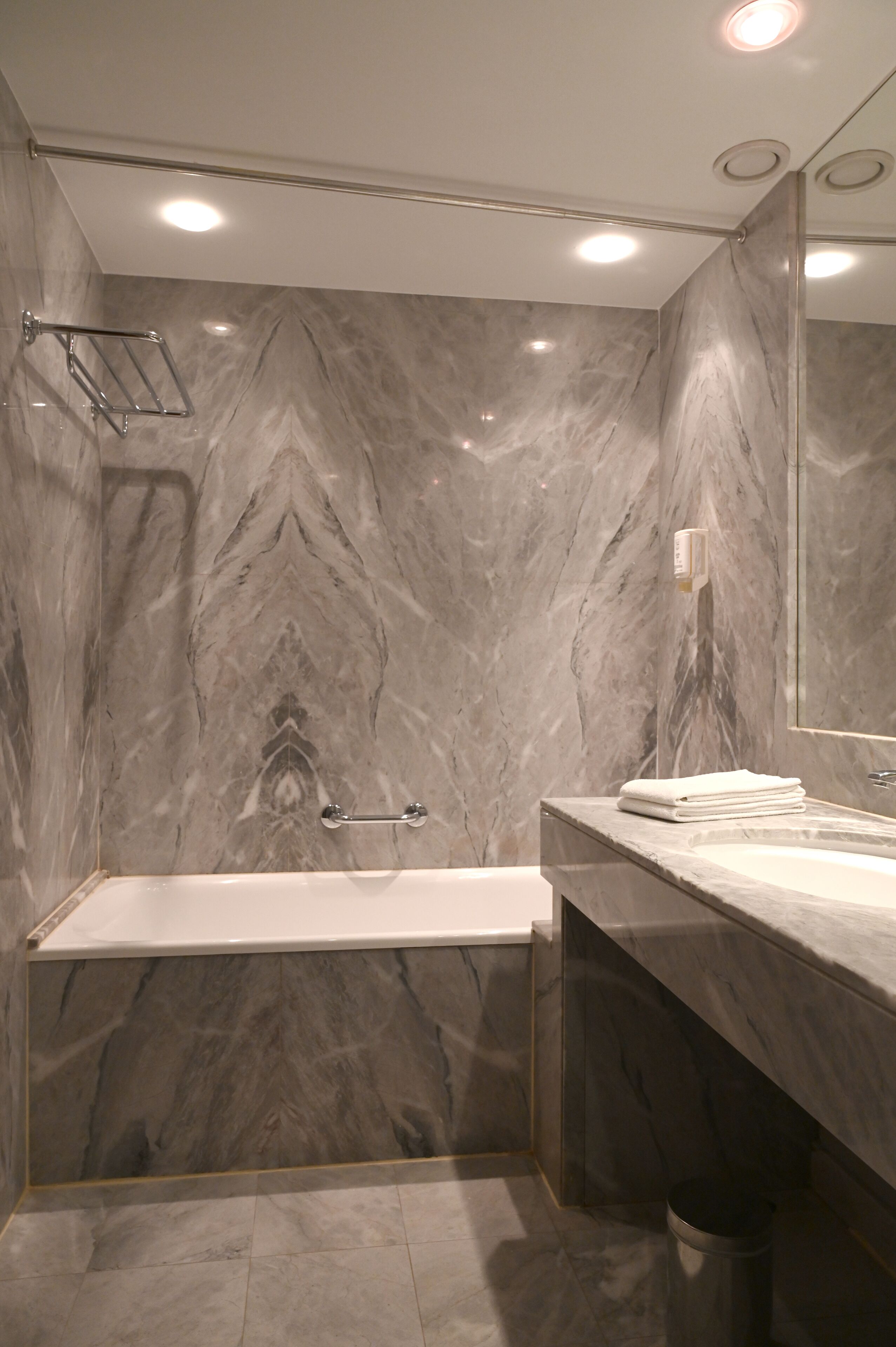 A modern bathroom with a marble wall, a bathtub, a sink, and a mirror.