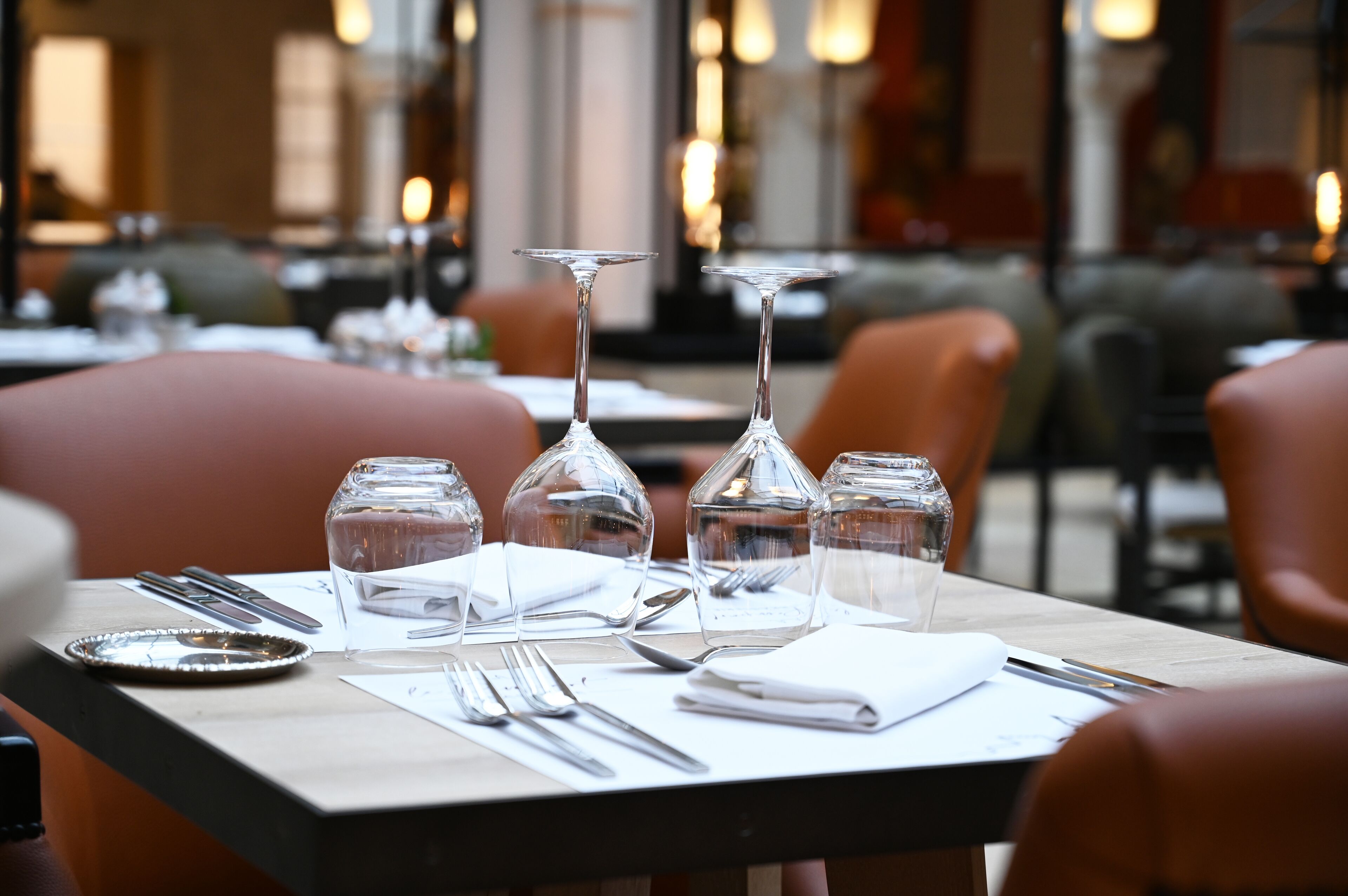 A dining table set with wine glasses, water glasses, cutlery, and a plate, in a restaurant with cushioned seating and a warm ambiance.