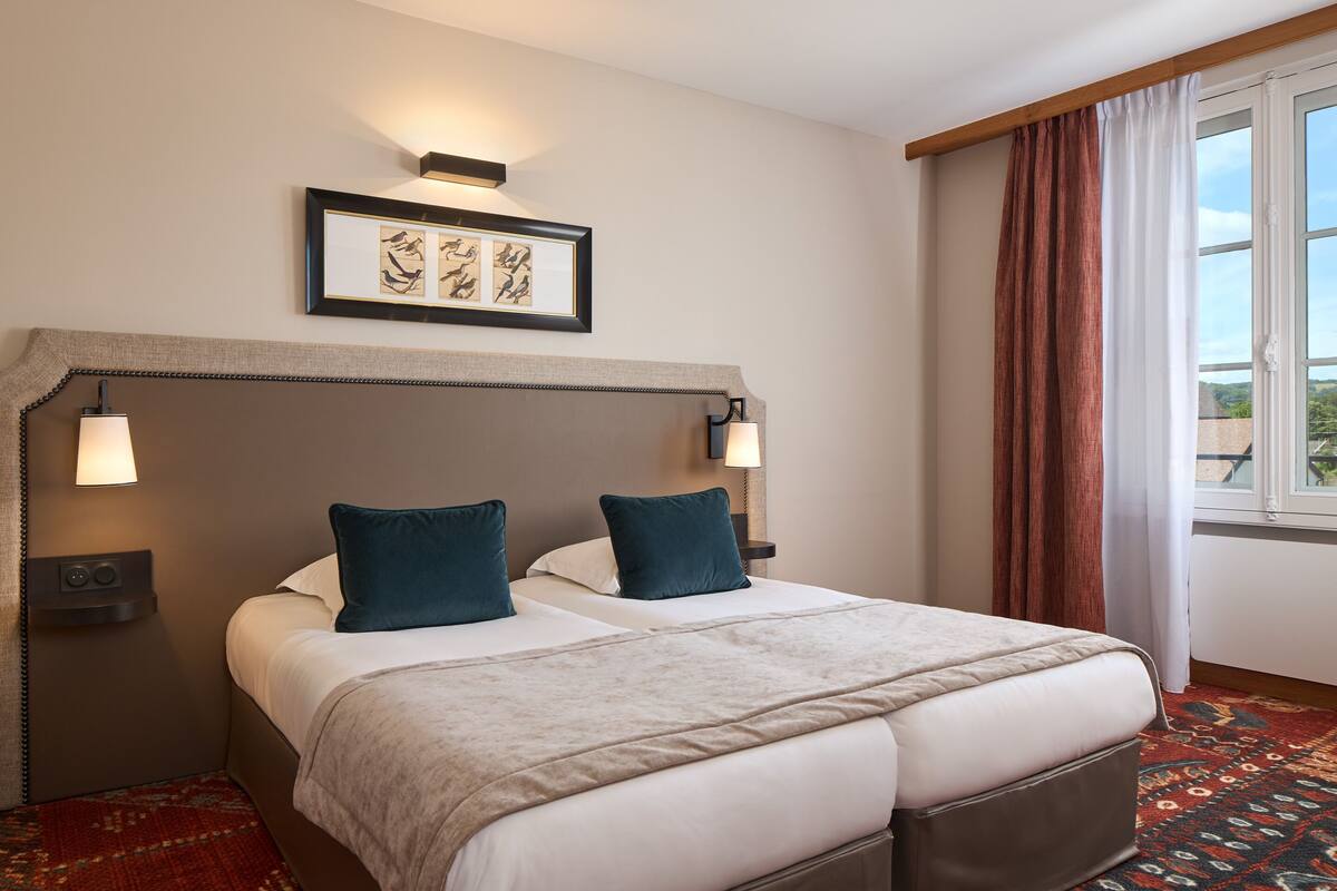 Une chambre d’hôtel avec un grand lit, deux lampes de chevet, un tableau encadré au-dessus du lit et une fenêtre avec des rideaux.