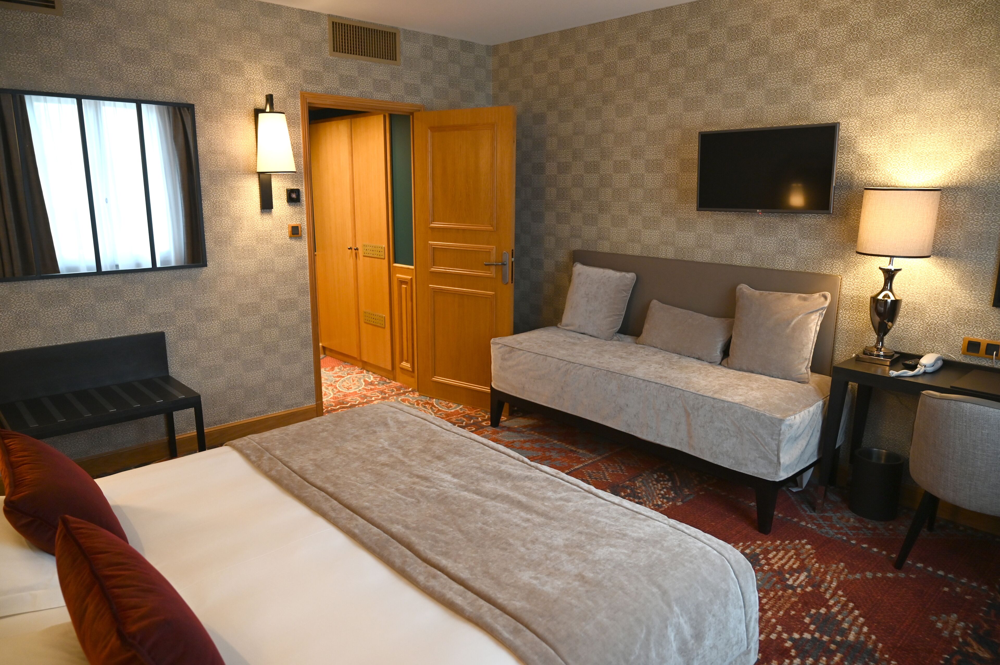 A hotel room with a bed, a sofa, a desk, a chair, a TV, and a wardrobe.