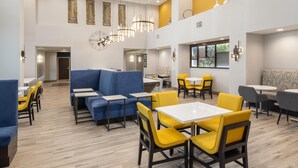 A modern restaurant with blue and yellow seating, white tables, and a chandelier. - Hampton Inn & Suites Manteca (Manteca)