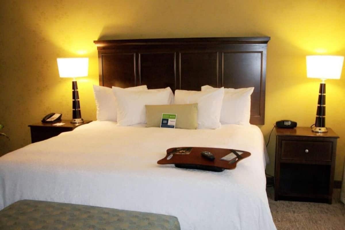 A hotel room with a large bed, two bedside tables, a bedside lamp, a tray with a remote control, and a small table with a phone.