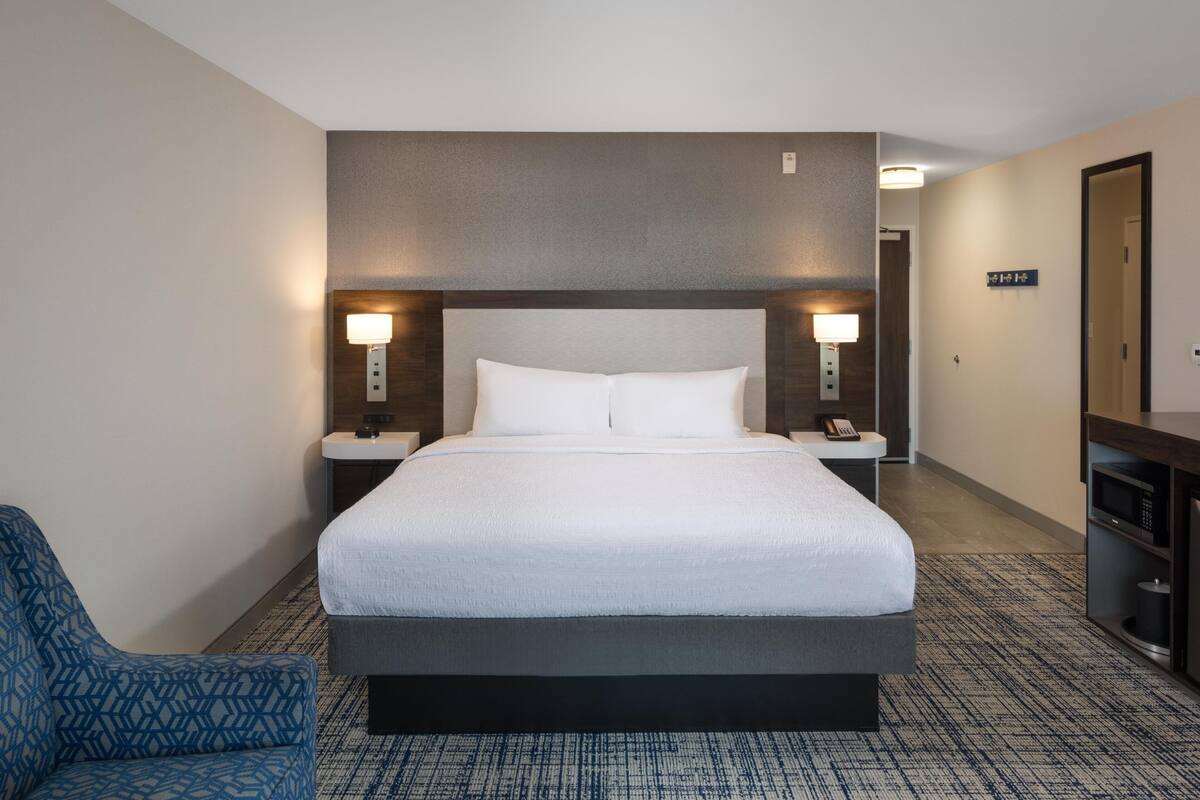 A hotel room with a large bed, bedside lamps, a desk with a chair, and a small bathroom.