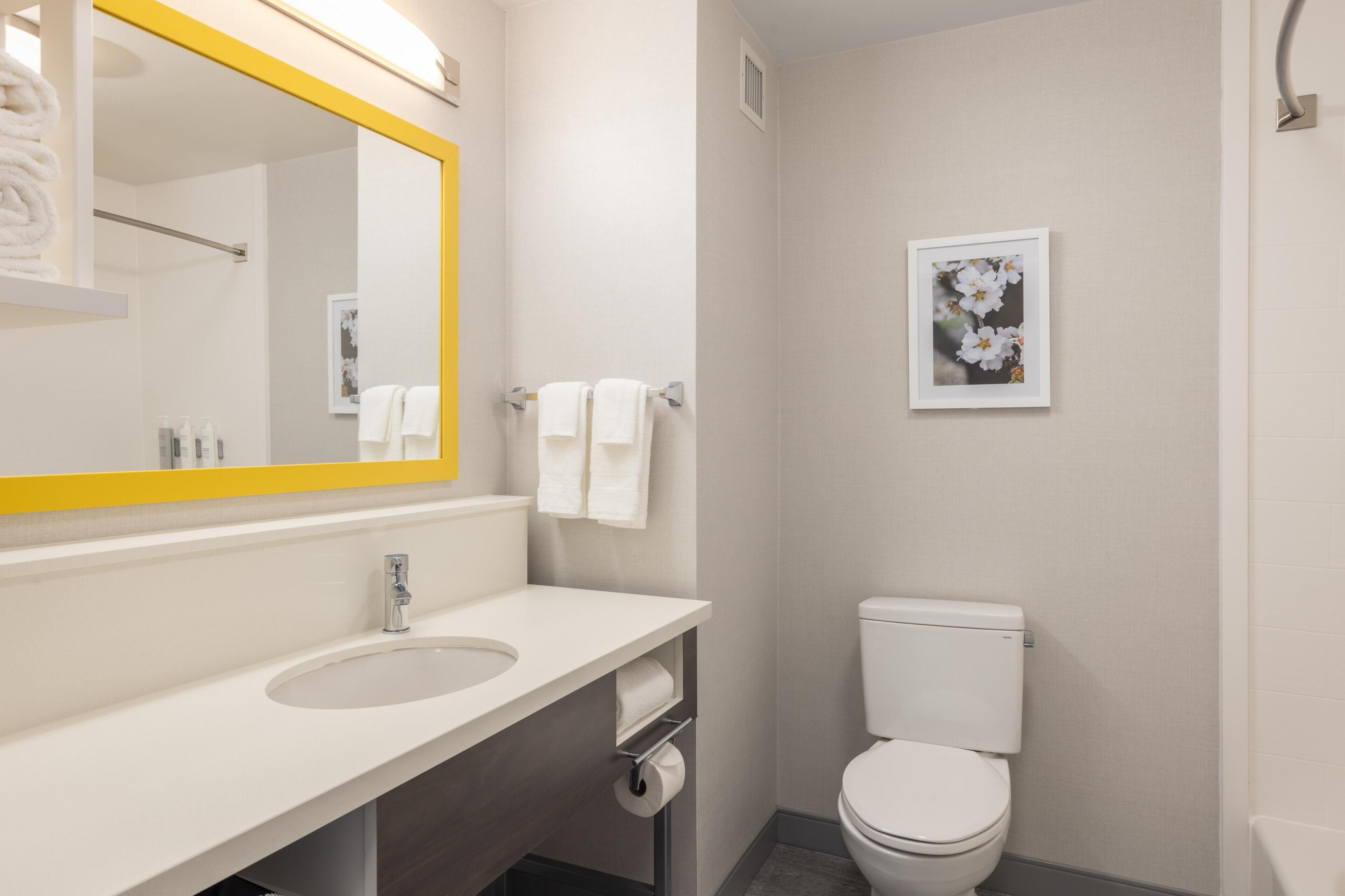A bathroom with a white sink, mirror, and toilet, with towels hanging on the wall.