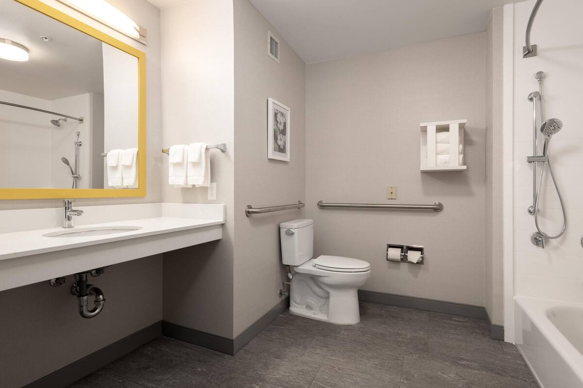 A modern bathroom with a sink, toilet, shower, and handrails.