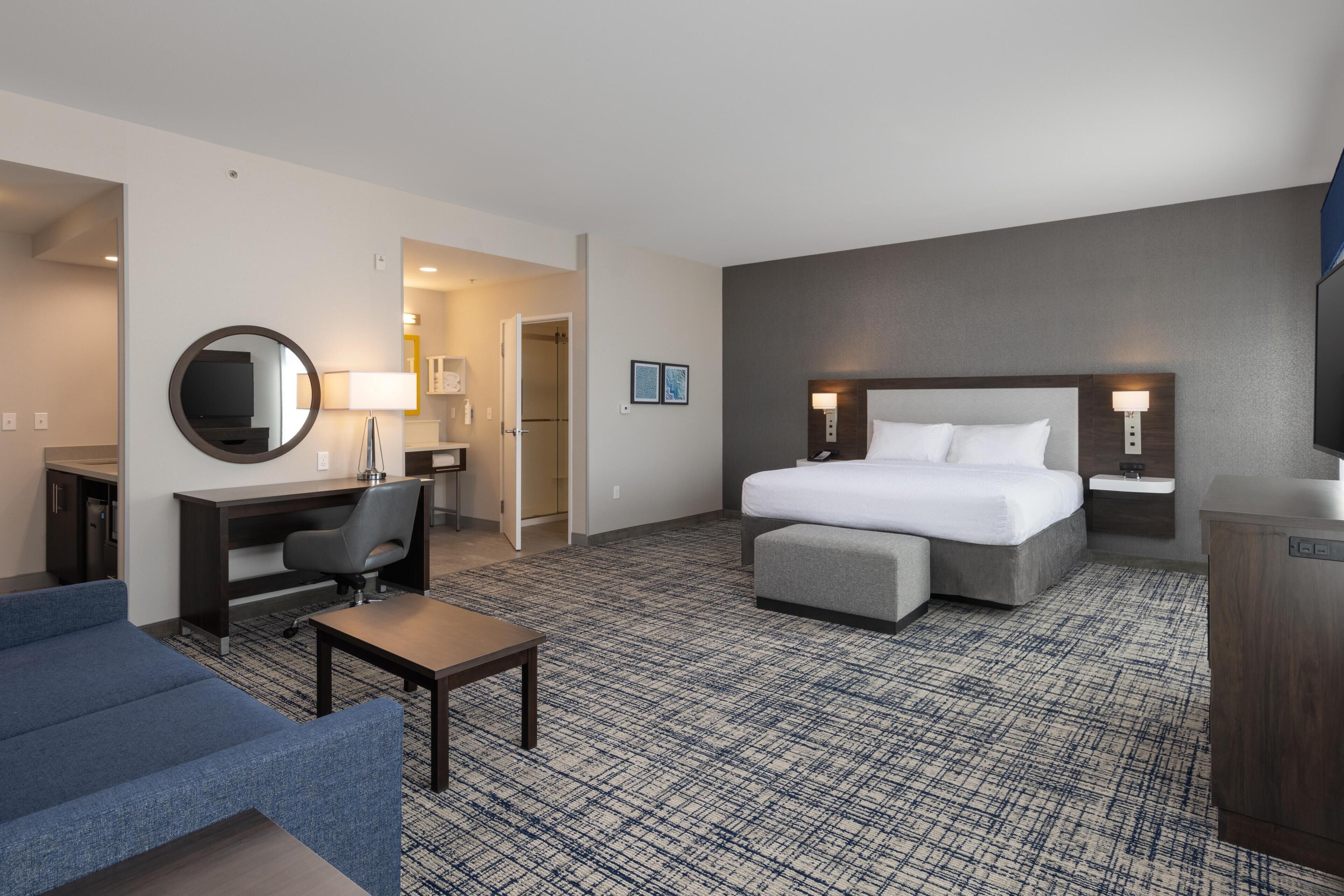 A hotel room with a bed, desk, chair, and a small table.