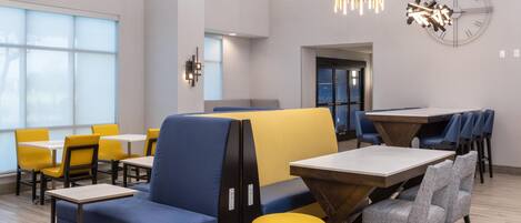 A modern dining area with high tables, blue and yellow seating, and pendant lighting.