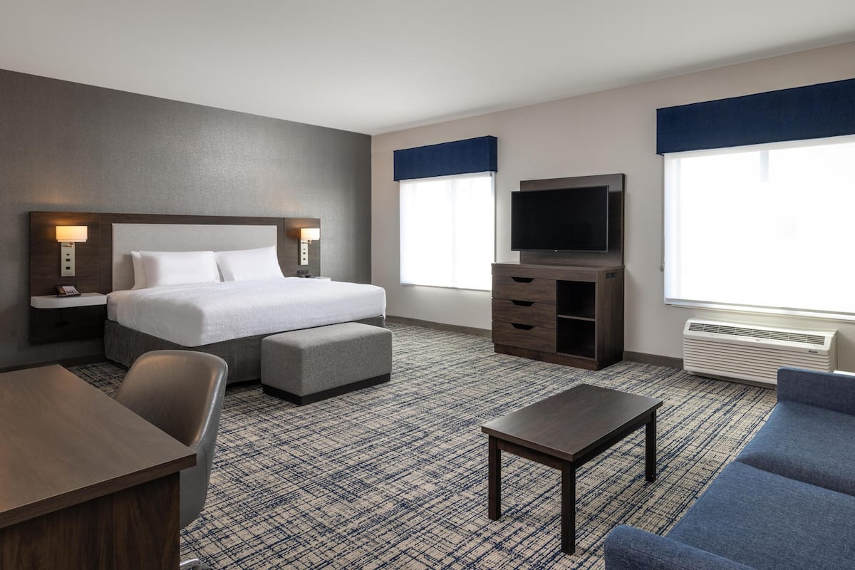 A hotel room with a bed, a TV, a desk, a chair, a sofa, and a carpeted floor.