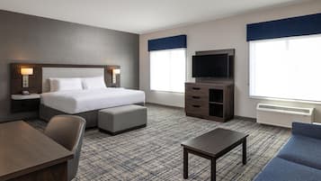 Habitación de hotel con cama, televisión, escritorio, silla, sofá y piso alfombrado.
