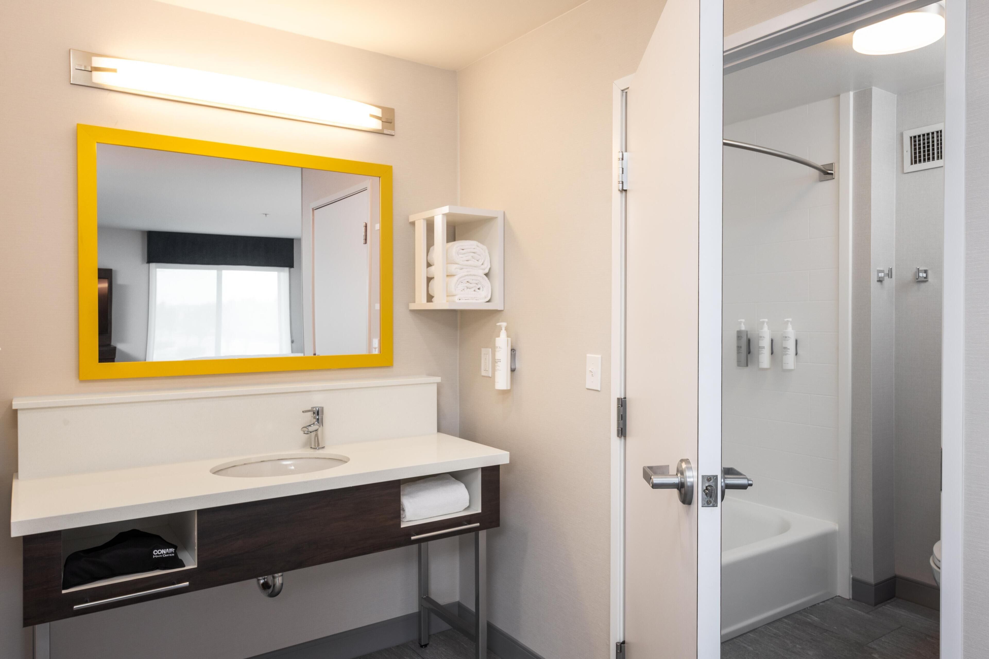 A modern bathroom with a white sink, a yellow-framed mirror, a glass shower enclosure, and a towel rack.