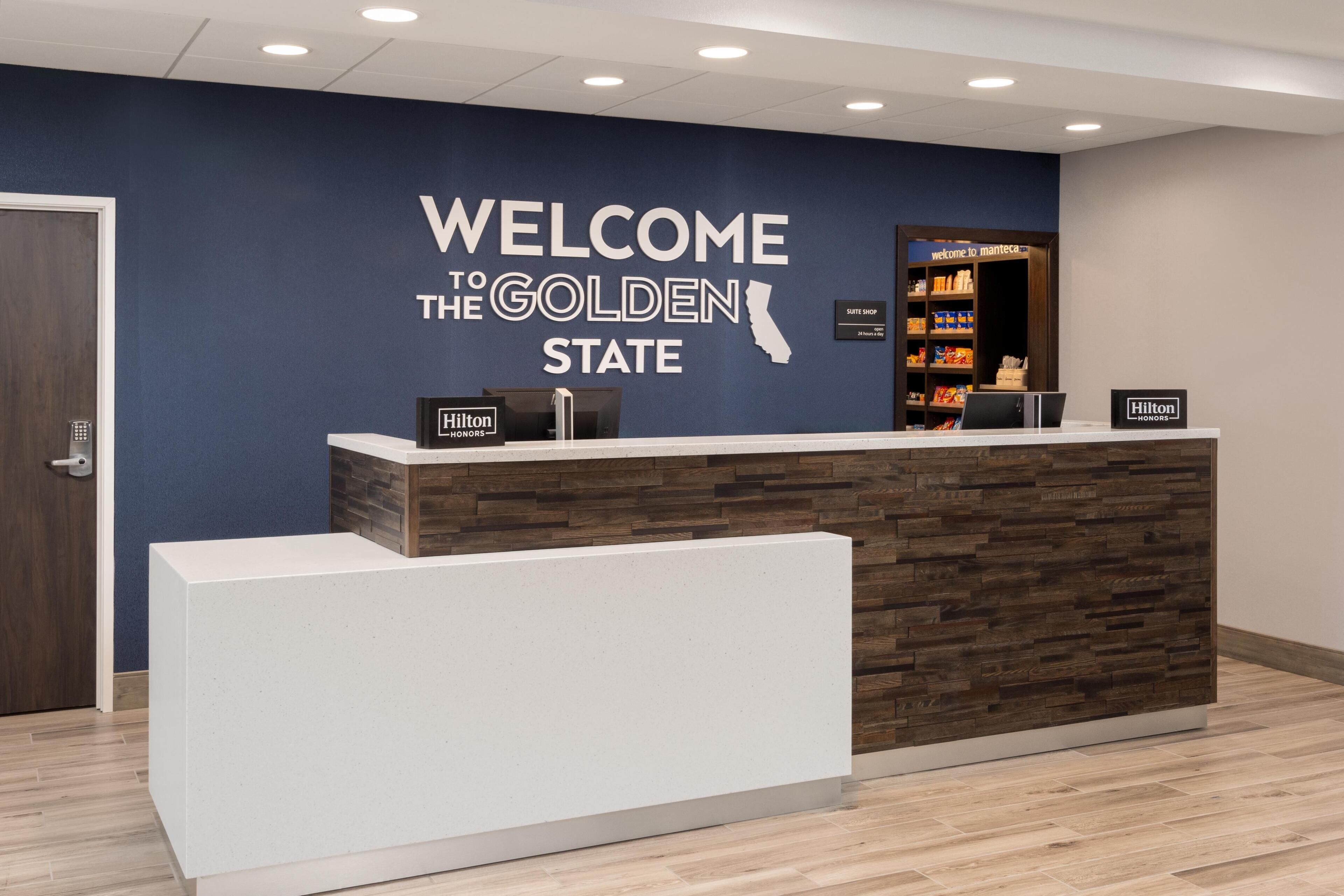 Un mostrador de recepción con un letrero que dice 'Welcome to the Golden State', un letrero de tienda de suites y un letrero de Hilton.