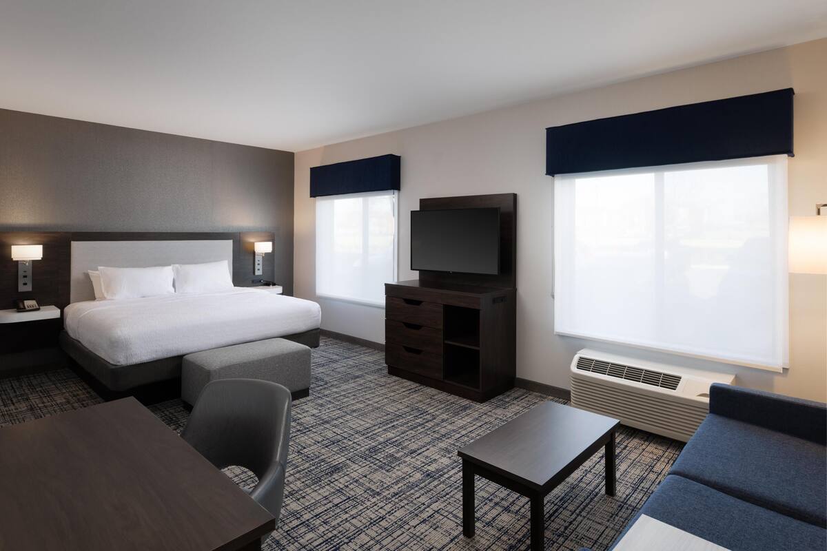 A hotel room with a bed, a desk, a chair, a TV, and a large window.