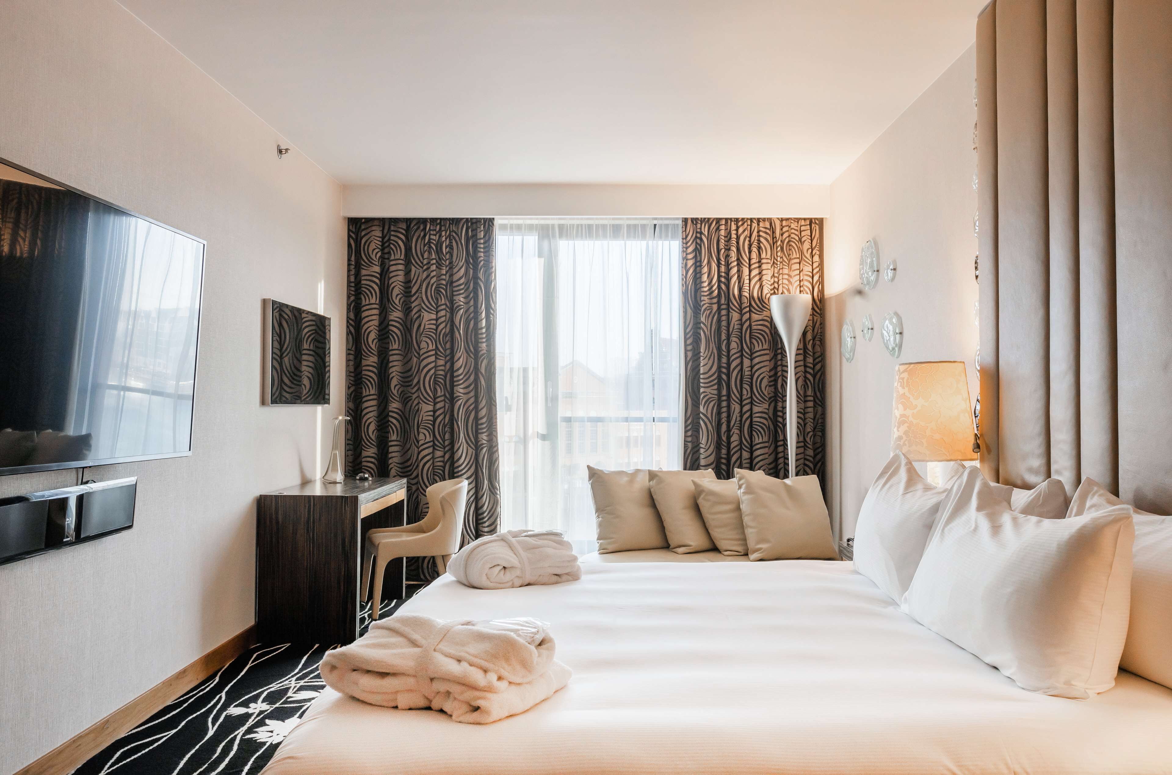 Een hotelkamer met een bed, een bureau, een stoel, een televisie en een raam met gordijnen.