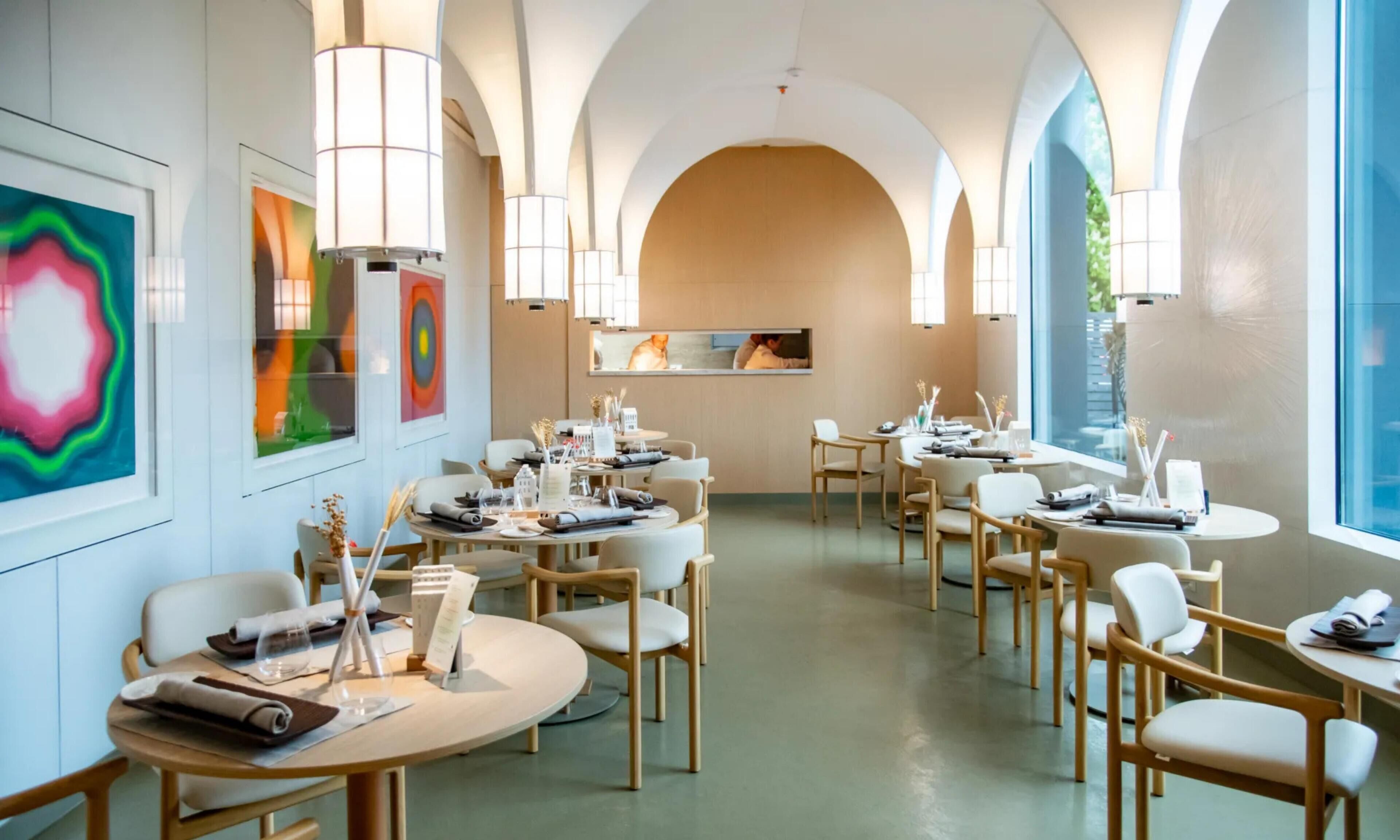 Un espace repas moderne avec des tables rondes, des chaises blanches et des œuvres d’art accrochées aux murs.