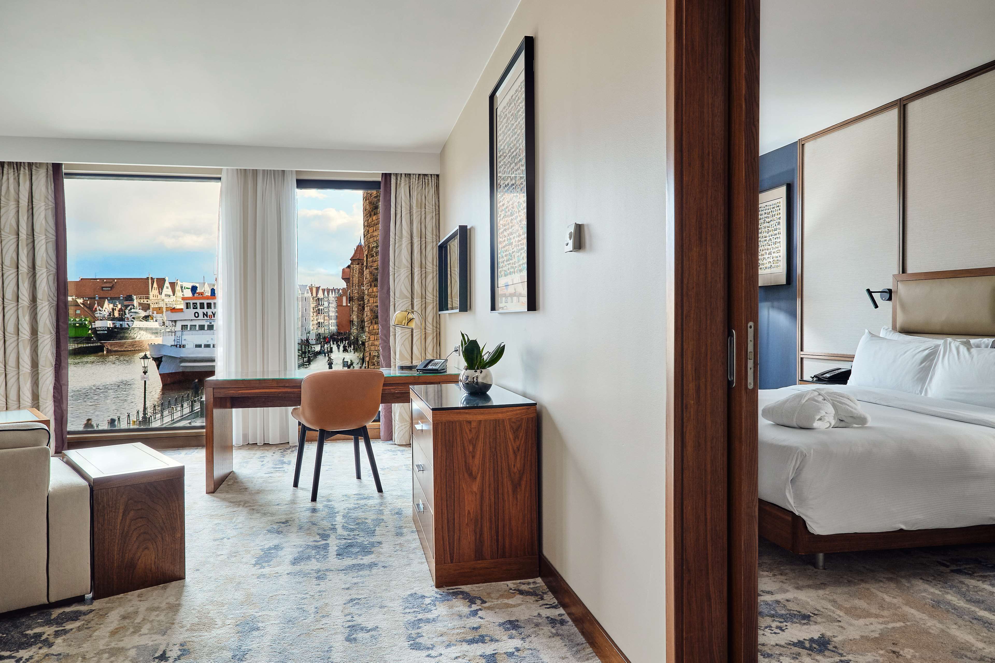 A hotel room with a bed, desk, chair, and a view of the city.