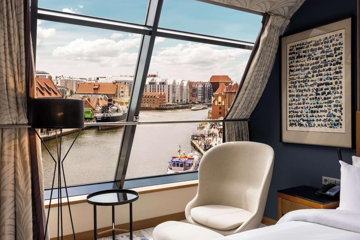 Quarto de hotel com uma janela ampla que oferece vista para um rio e paisagem urbana.
