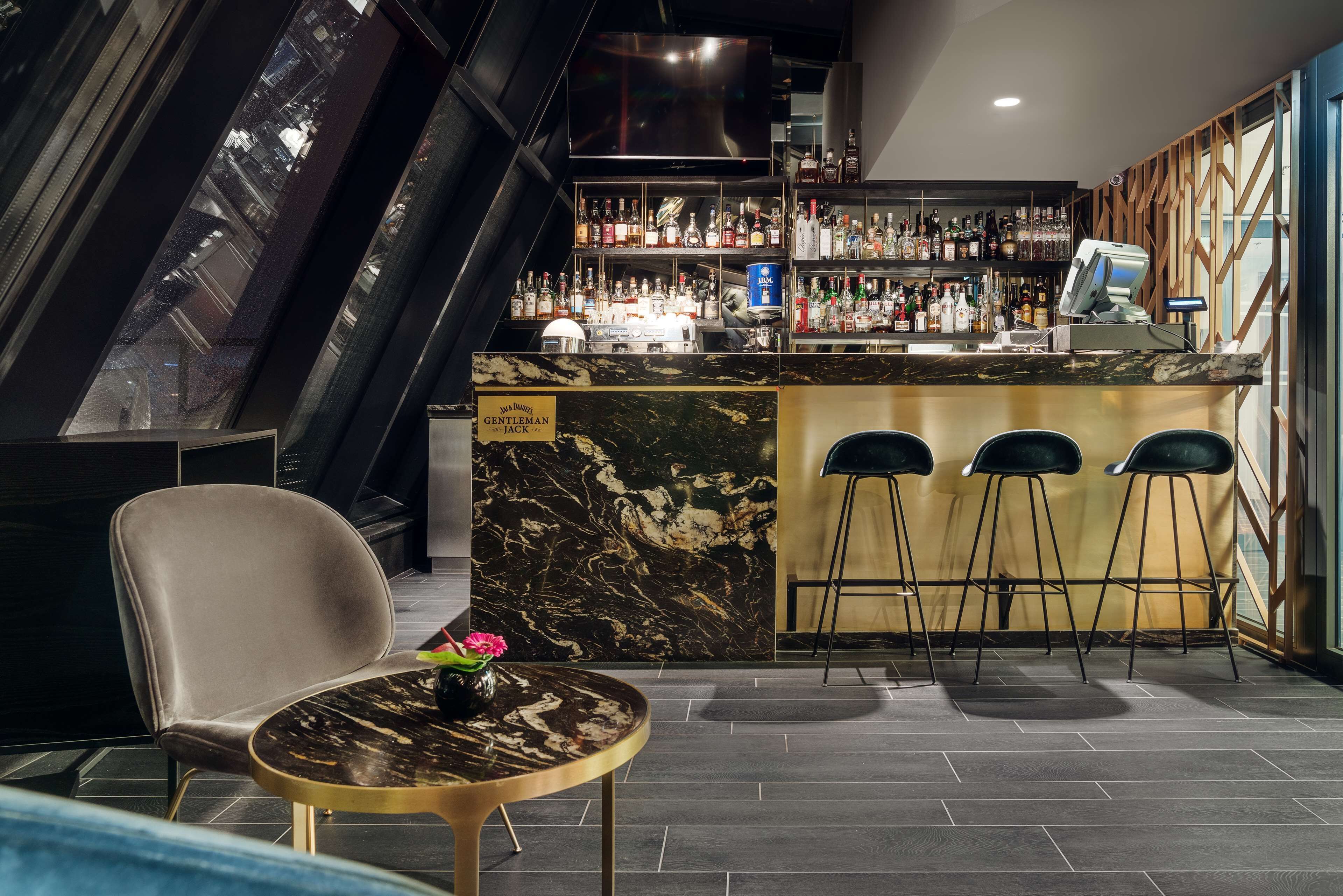 A bar area with a marble countertop, bar stools, and a variety of liquor bottles.