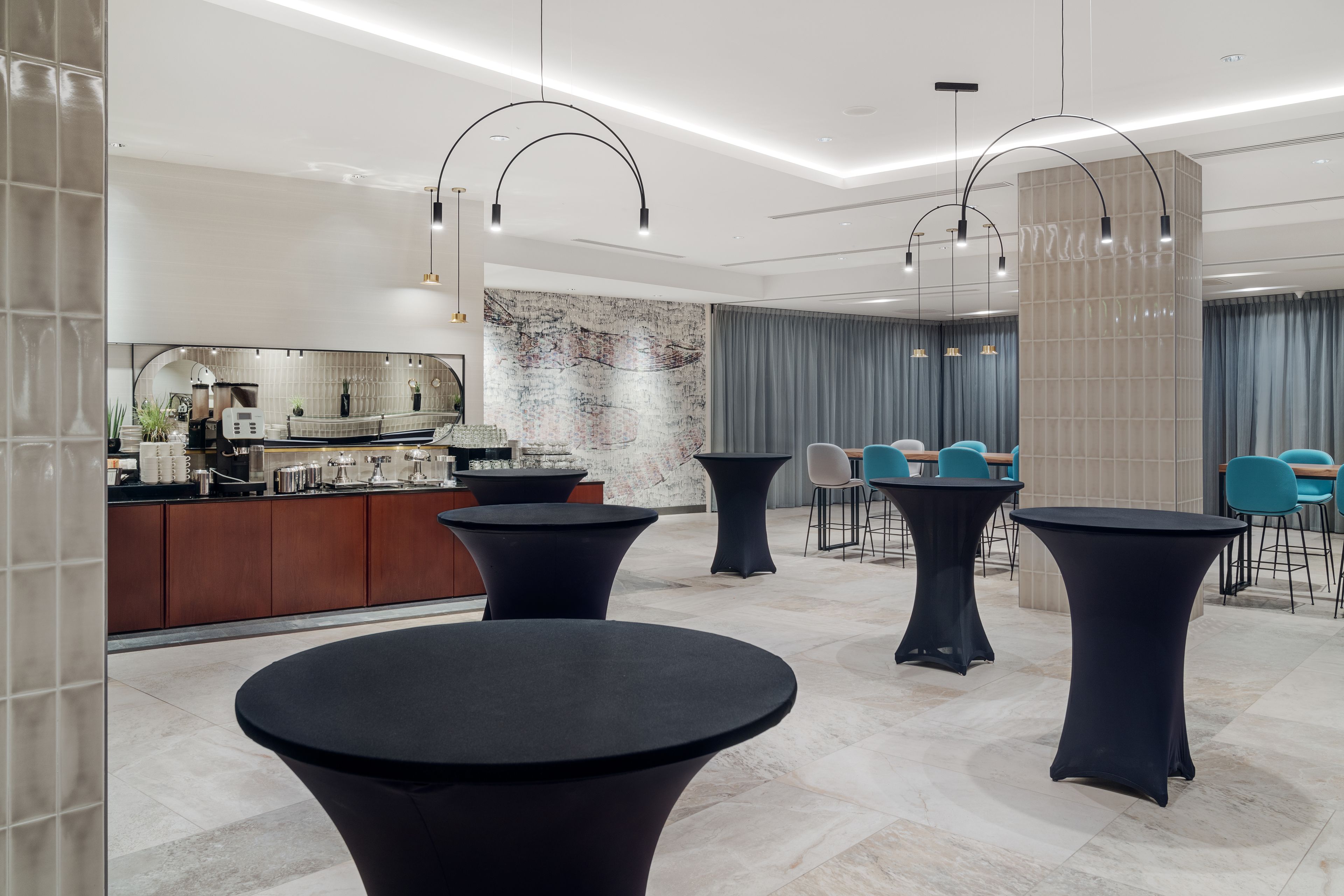 A modern hotel lobby with round tables, a bar area, and a large abstract painting on the wall.
