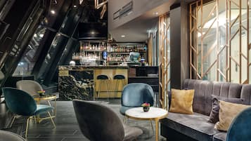 A modern bar area with a marble countertop, bar stools, and a seating area with a sofa and chairs.