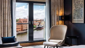 Een hotelkamer met een groot raam, een stoel, een bed en een lijst met een kunstwerk aan de muur.
