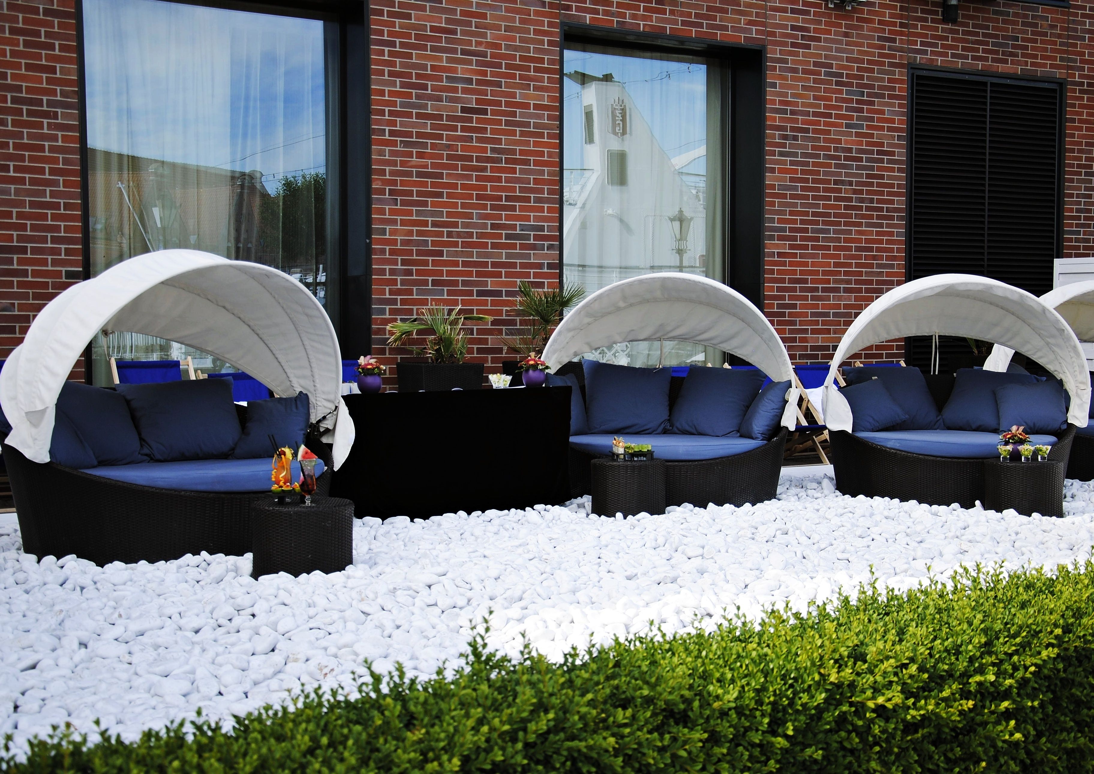 Three outdoor seating areas with white canopies, blue cushions, and a white pebble ground cover.