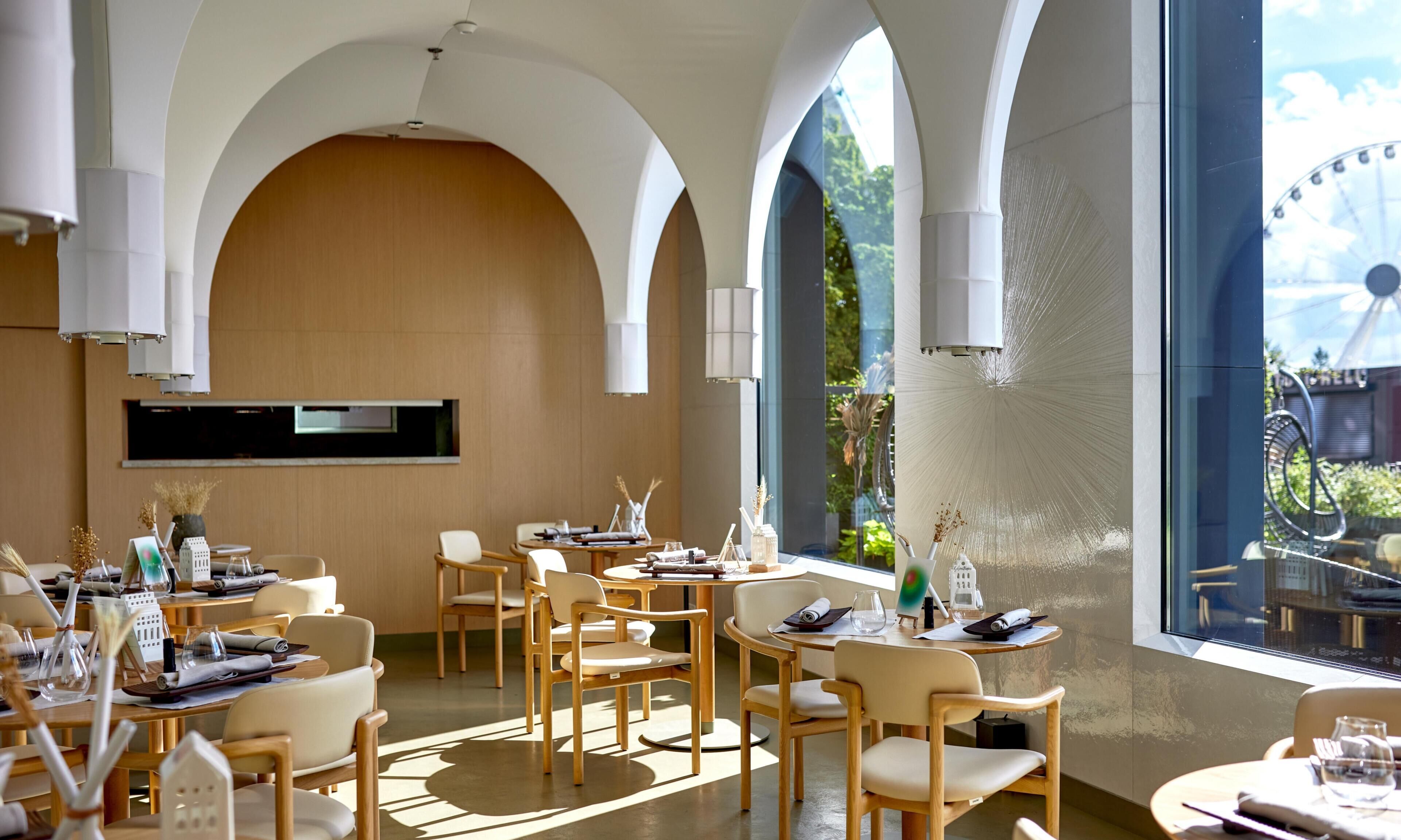 A restaurant with high arched ceilings, wooden furniture, and large windows offering a view of greenery.
