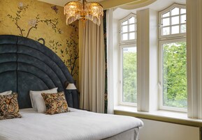 Un dormitorio con una cama grande, una araña y una ventana con vistas a árboles.