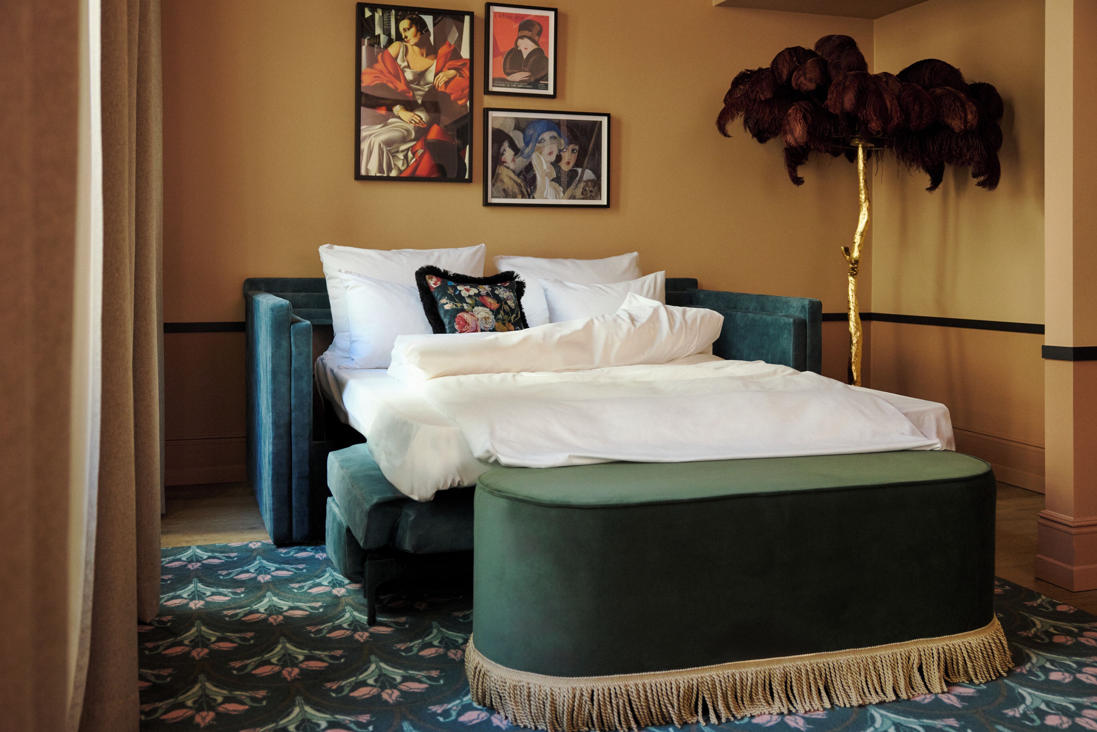 Un dormitorio ordenado con una cama, un reposapiés verde y dos obras de arte enmarcadas en la pared.