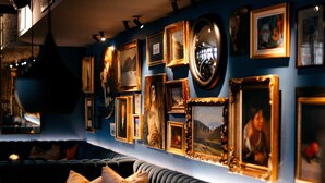 A room with a blue wall adorned with various framed artworks, a blue sofa, and a radiator.