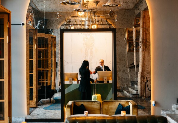 A lobby with a reception desk, a seating area with a sofa, and a large mirror reflecting the interior.