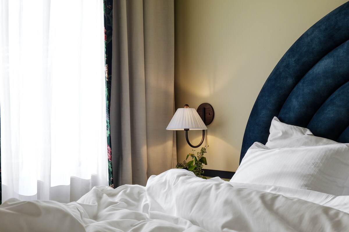 A neatly made bed with white linens, a wall-mounted lamp, and a dark blue headboard.