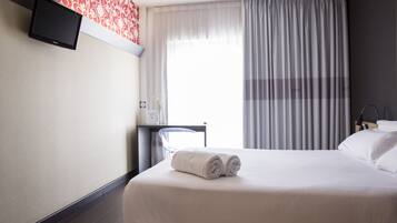 Een hotelkamer met een bed, een bureau, een stoel en een aan de muur bevestigde televisie.