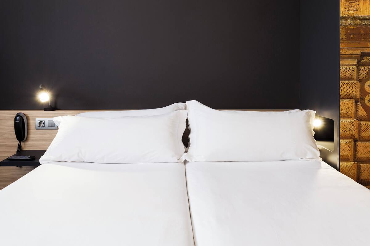 A neatly made bed with white linens, a bedside table with a lamp, and a phone.