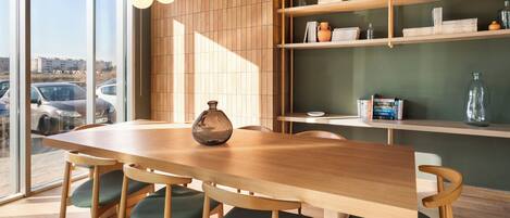 Un comedor moderno con una mesa y sillas de madera, un florero sobre la mesa, y una estantería con libros y objetos decorativos.