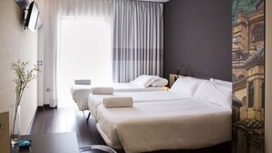 A hotel room with two beds, a desk, a chair, a vase with flowers, and a painting on the wall. - B&B Hotel Granada (Pulianas)