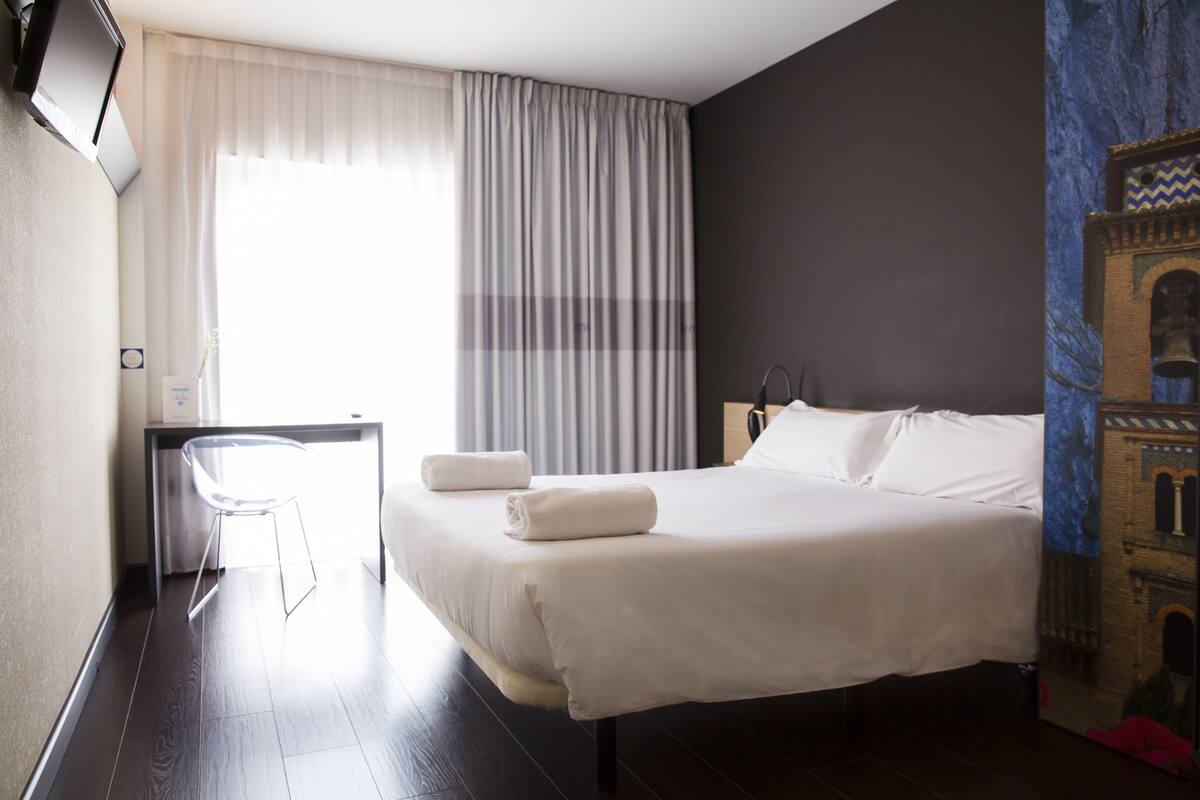 A hotel room with a bed, a desk, and a chair.