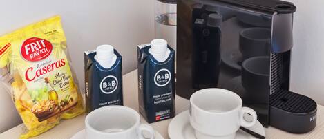 A breakfast setup with two white cups, a bag of Frit Ravich Caseras chips, two B&B Hotels milk cartons, and a coffee maker.