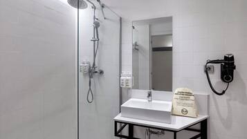 Ein modernes Badezimmer mit einer gläsernen Duschkabine, einem weißen Waschbecken und einem an der Wand befestigten Föhn.