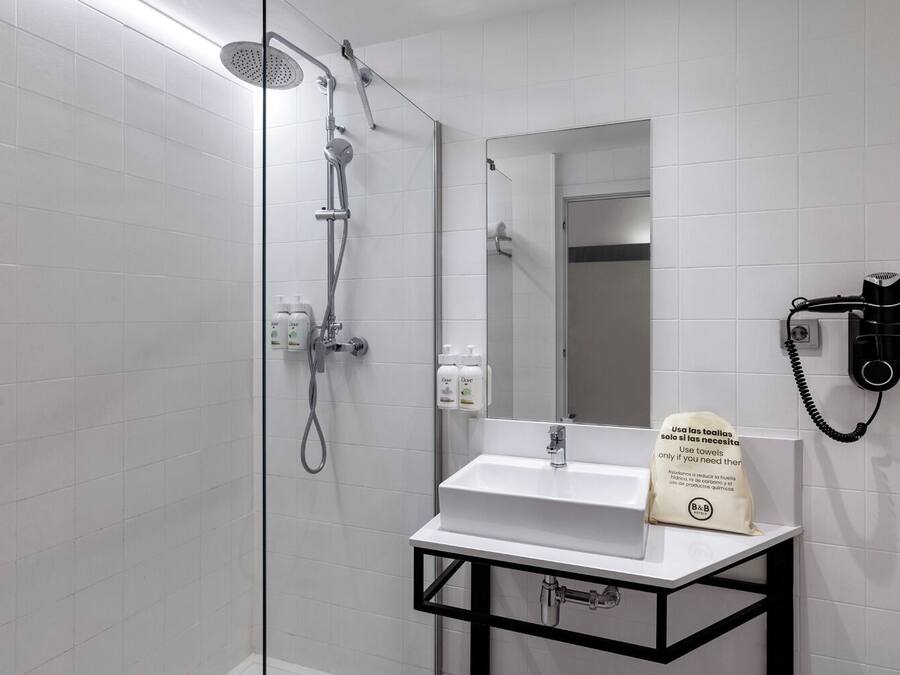 Un baño moderno con ducha envuelta en vidrio, lavamanos blanco y secador de pelo montado en la pared.