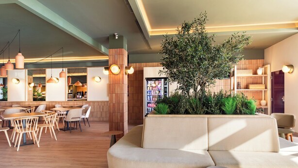 A modern hotel lobby with a curved sofa, wooden tables, and hanging pendant lights. - B&B Hotel Granada (Pulianas)