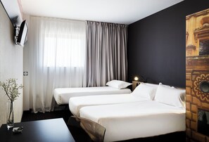 A hotel room with two beds, a desk, a vase with flowers, and a wall-mounted TV. - B&B Hotel Granada (Pulianas)